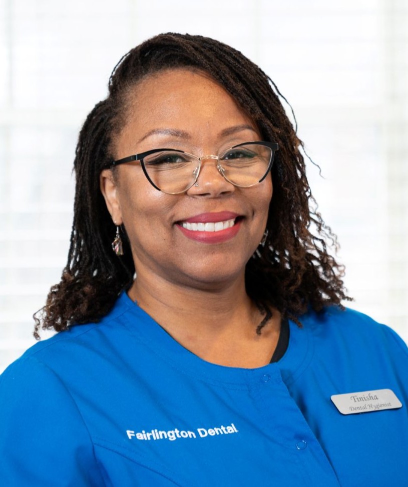 Smiling Black woman in blue dental scrubs with a name badge reading Timisha, a dental hygienist at Fairlington Dental.